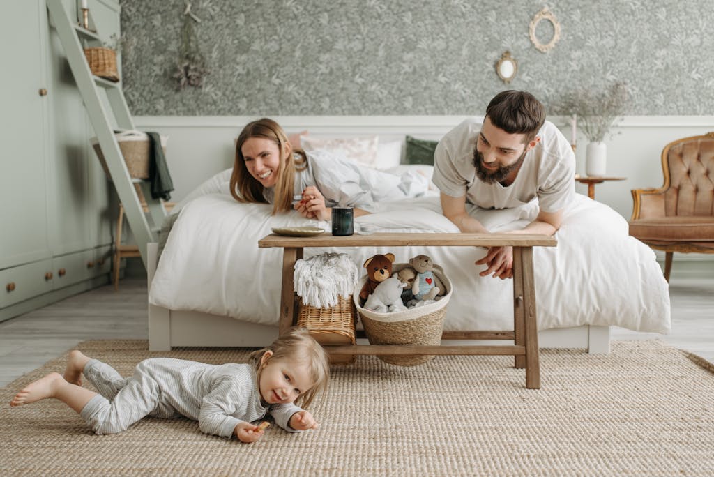 A Couple Lying on the Bed while Looking at Their Daughter Crawling on the Floor